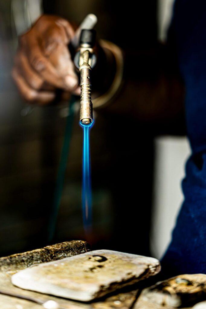 Close-up of a hand holding a torch during the process of jewellery soldering.